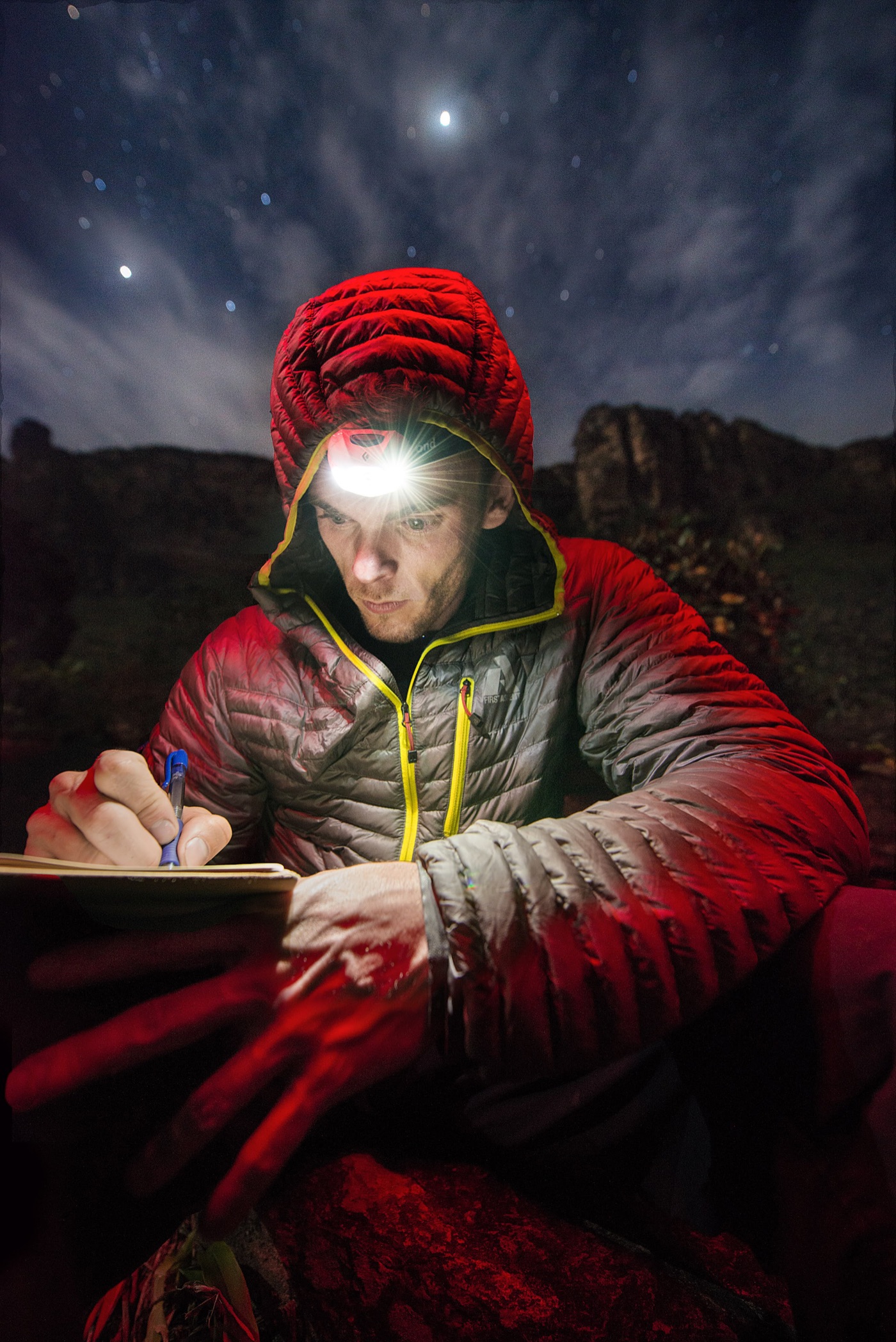 A climber in a red down jacket writing by headlamp under the night sky on the tepui