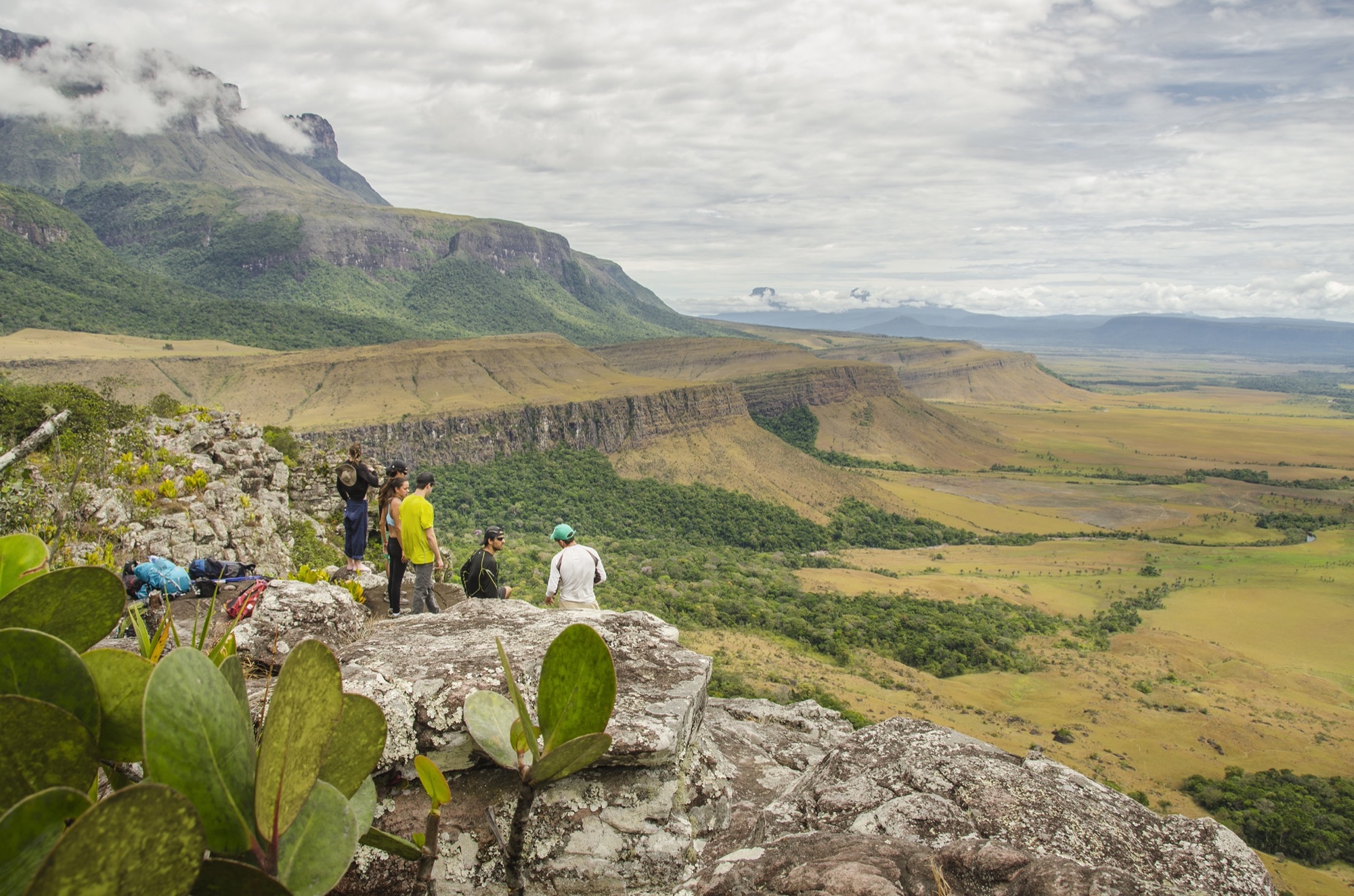 A small group of trekkers on a rock ledge above the Gran Sabana, a tepui wall behind them